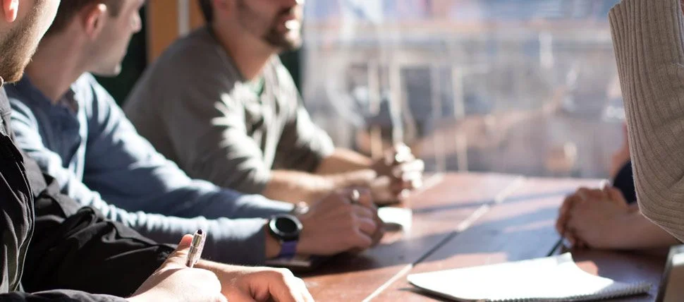 close up of hands taking notes and several people at a table